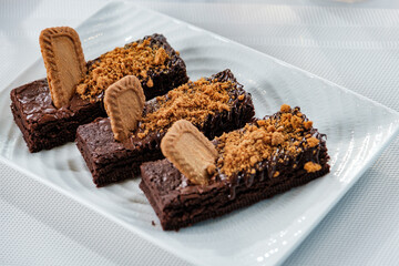 A decadent chocolate brownie sits on a white plate, accompanied by a steaming cup of English tea. The white tablecloth is spotless, adding to the elegant atmosphere.