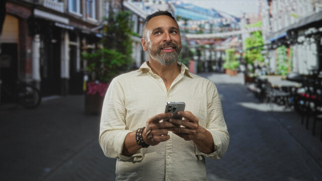 Man holding smartphone with both hands and smiling while looking up on a street; contentment curiosity connection.