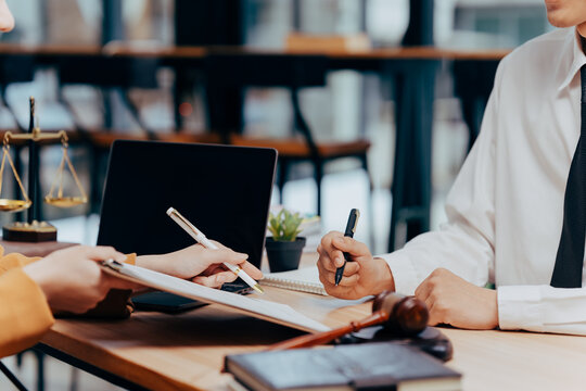 Legal Agreement: Two professionals, engaged in a discussion over the terms of a contract, captured with the presence of a laptop, scales and gavel.