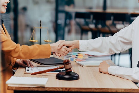 Legal Agreement Handshake: An agreement is sealed with a firm handshake between two individuals at a wooden table, with the gavel and scales of justice laid out in the background.