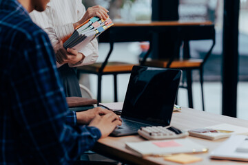 Work Collaboration: Two individuals engage in focused teamwork, a laptop on the desk acts as the...