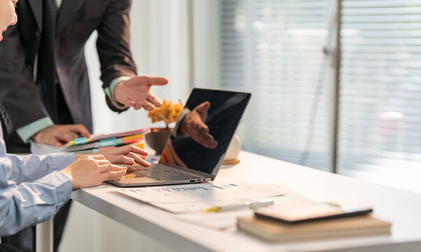 Collaboration in the Workplace: Two professionals, deep in discussion, gather around a laptop, immersed in collaborative work, data, charts, and diagrams, exemplifying business strategy and teamwork.
