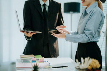 Collaboration in the Corporate World: Two individuals, dressed in business attire, engage in a focused discussion, each holding technological tools, which shows effective teamwork.