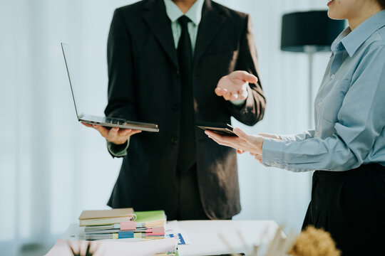 Business Discussion: A professional scene where a man and a woman in business attire engage in a focused discussion, possibly reviewing a laptop and documents.