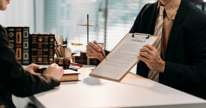 Legal Contract Review: Two professionals engage in a focused discussion as a document is presented, underscored by the presence of a balanced scale symbolizing justice and legal accuracy. - Powered by Adobe