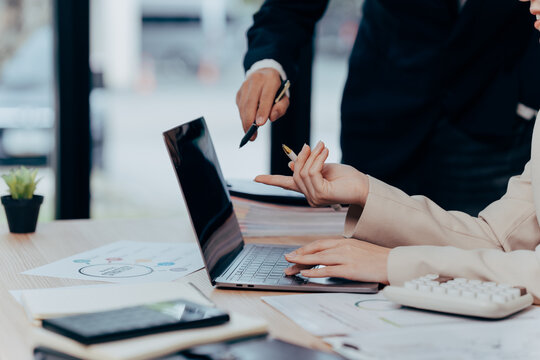 Business Collaboration: A pair of professionals collaborate at a desk, a laptop open, amidst paperwork and office supplies, highlighting teamwork and productivity.