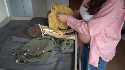 Pregnant woman sorting baby clothes indoors - Powered by Adobe