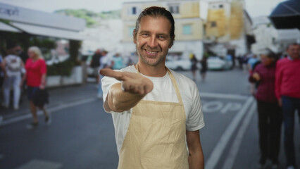 Naklejka premium Smiling blond man with long hair wearing apron extends hand on street; welcoming hospitality generosity community.