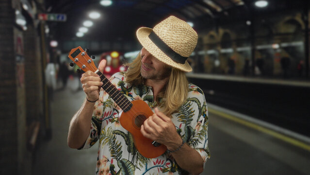 Blond man with straw hat and floral shirt strumming ukulele in an underground building; creativity serenity.