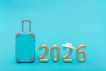 Golden numbers 2026 with suitcase and hat on blue background. Symbol of travel, new year, vacation and future journey.