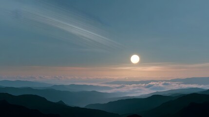 Fototapeta premium Serene layers of misty mountains at sunrise or sunset with a luminous sun in a vast atmospheric sky filled with soft clouds
