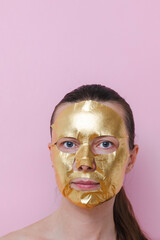 A woman with a golden facial mask against a pink background. The image represents self‑care, beauty and personal wellness. Vertical photo