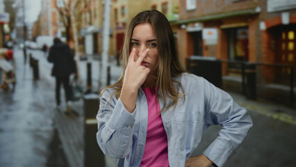 Fototapeta premium Woman outdoors making a watchful gesture on a city street, expressing vigilance and attention, with a blurred background suggesting urban life and dynamic surroundings.