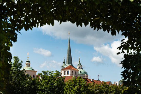Prague, Czech Republic &ndash; August 6, 2025: Baroque domes and spire of St Thomas Church and St Nicholas Church framed by foliage in the Wallenstein Garden, Prague, Czech Republic