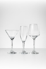 Three empty glassware pieces—a martini, champagne, and wine glass—are neatly arranged on a white surface against a light background, showcasing elegant shapes and crystal clarity.