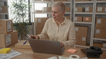 Woman at desk with stacked parcels and laptop, holding phone and raising hands in building while...