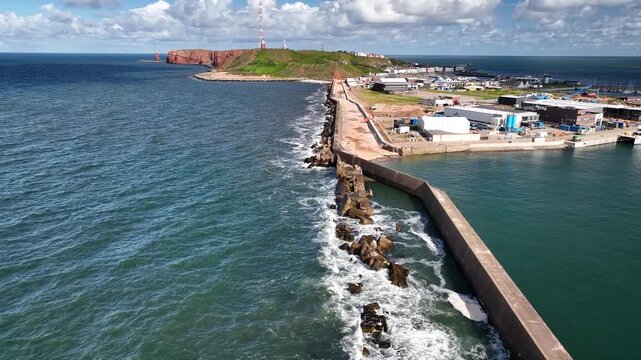 Aerial footage of offshore island Heligoland in German Bight with the breakwater protecting  harbor, the turquoise North Sea, and red cliffs leading toward sea stack Lange Anna. 