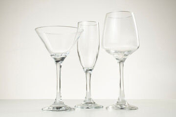 Three empty glass cups including wine, champagne, and martini glasses on light background.