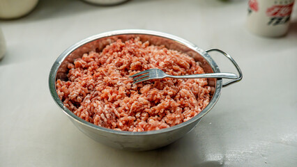 Raw ground meat in metal bowl with fork, overhead view. Fresh minced beef perfect for cooking and recipe content. Professional food photography for culinary, meal prep, and kitchen themes.