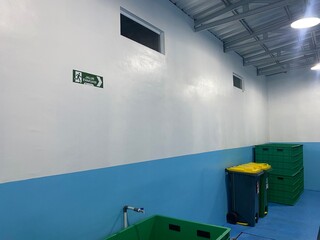 Indoor facility with white walls, blue lower section, and green recycling bins, showcasing a clean and organized space for waste management