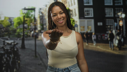 Fototapeta premium Woman with outstretched hand reaching forward on sunlit city street, smiling gently; invitation warmth.