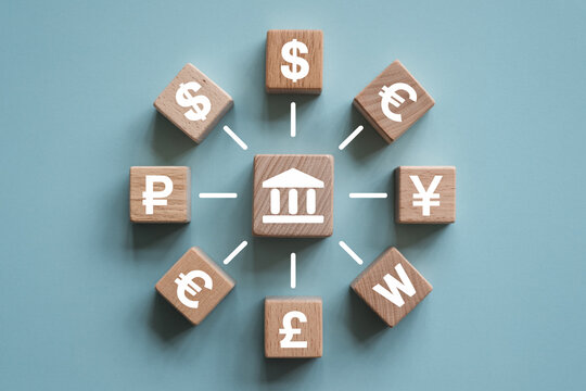 Wooden blocks displaying global currency symbols including the dollar euro yen and pound arranged around a central block with a bank icon symbolizing international finance and banking concepts