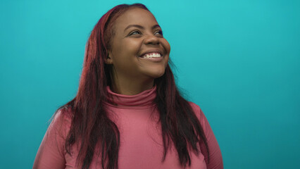 Woman smiling with visible teeth in pink turtleneck in studio with teal background; optimism future...