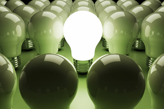 Illuminated lightbulb stands out among unlit bulbs on a green surface symbolizing innovation creativity and a bright idea in a conceptual representation of leadership and uniqueness