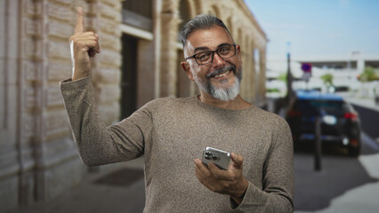 Man holding smartphone points finger up on street near parked car; confidence connection curiosity.