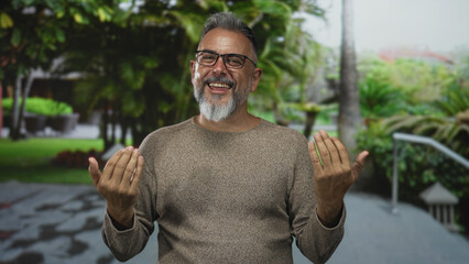 Middle aged man with glasses and beard smiling, hands open, gesturing on a forest pathway in a park; friendly welcoming joy.