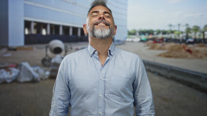 Fototapeta premium Man smiling with head tilted back showing grey beard and bare neck at building site with cement mixer and sand piles visible; quiet contentment.