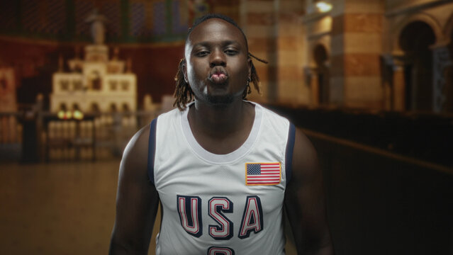 Man puckers lips in usa basketball jersey with american flag patch, bare shoulders visible inside catholic church nave; community playful joy. - Powered by Adobe