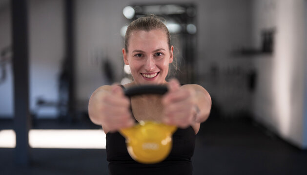 Woman exercises with yellow kettlebell in gym during daytime, showcasing strength and fitness routine - Powered by Adobe
