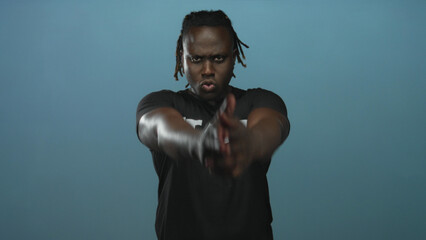Man pointing both hands forward in blue studio with intense stare and black staff t shirt visible;...