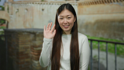 Woman smiling and waving in front of ancient roman ruins outside on city street.