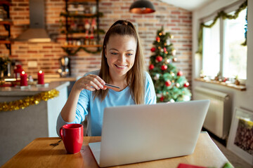 Young adult woman smiling and shopping online at home during christmas