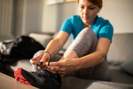 Young adult woman lacing running shoes at home, focused