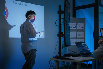 young Asian software development manager leads a late-night office discussion with his executive team, mentoring developers and analyzing source code to guide programming and project development