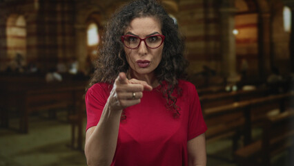 Woman in red shirt finger pointing to camera in church building with stern expression; anger rebuke admonition warning.