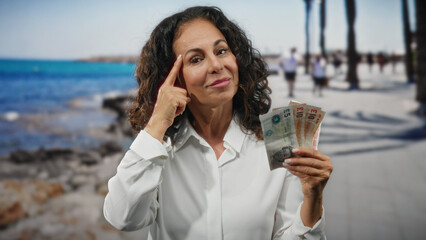 Woman holding british pound banknotes on a sunny seaside promenade, exuding confidence in a leisure setting by the beach.