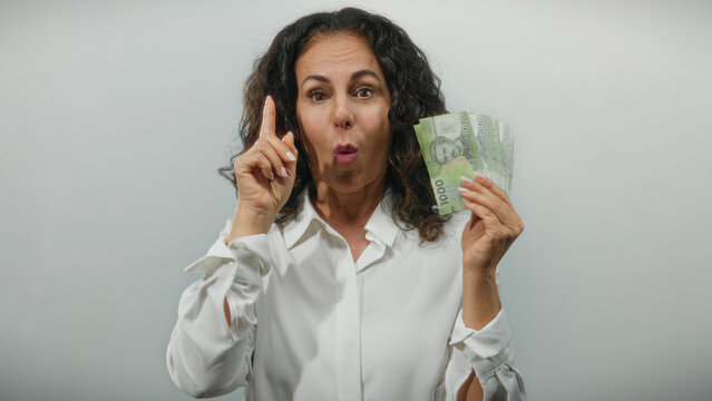 Middle-aged woman holding chilean pesos makes a thinking gesture against a white background, symbolizing financial decision-making and ideas. - Powered by Adobe