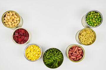 Open cans of beans, mushrooms, carrots, corn, peas, green beans, lentils, asparagus, and olives on a white background with copy space.