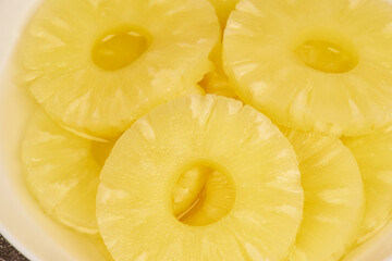 Sliced ​​pineapple, canned preserve. Close-up photograph with copy space on a table against a rustic background.