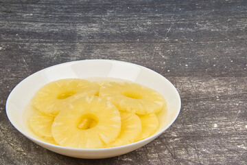 Sliced ​​pineapple, canned preserve. Close-up photograph with copy space on a table against a rustic background.