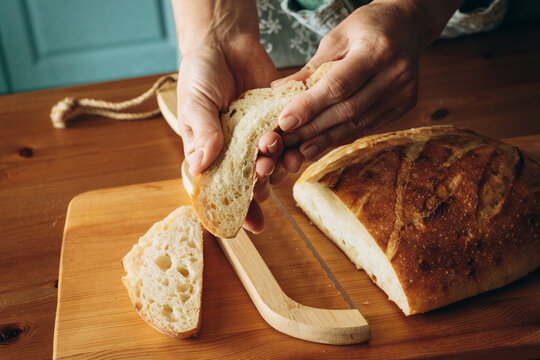 Hands breaking fresh sourdough bread on wooden cutting board in kitchen
