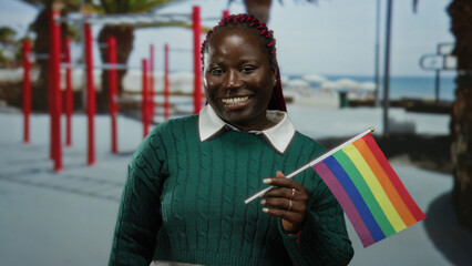 Woman smiling with rainbow flag in outdoor sports center with palm trees highlighting lgbt pride and diverse inclusivity in a vibrant gym setting.