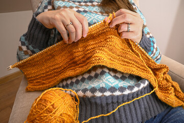 Woman knitting a warm sweater with orange yarn, enjoying a cozy hobby at home