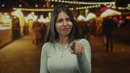 Young woman pointing finger at camera and tapping temple on crowded street; doubt suspicion confusion.