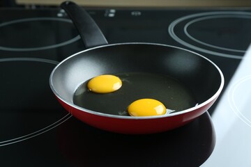 Frying pan with raw chicken eggs on cooktop in kitchen, closeup