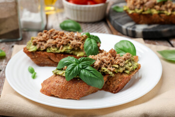 Delicious bruschettas with tuna, avocado and basil on table, closeup